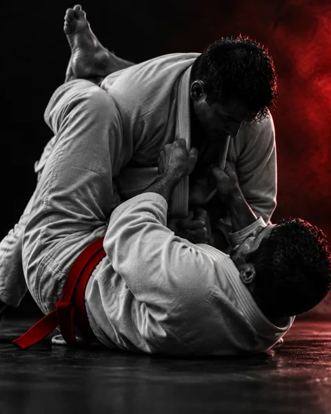 Dos practicantes de jiu-jitsu brasileño (bjj) con kimono luchando en el suelo por una sumisión