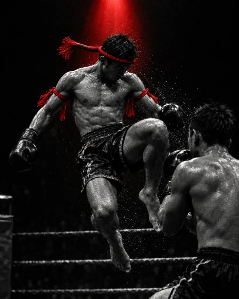 Luchador de muay thai con mongkon en la cabeza lanzando un rodillazo en el ring