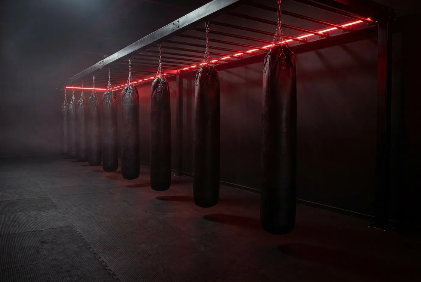 Fila de sacos de boxeo colgados bajo una tira de luz roja