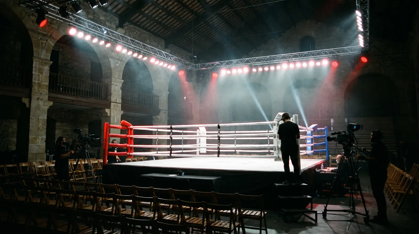 Ring de boxeo montado en un pabellón con focos y cámaras de televisión