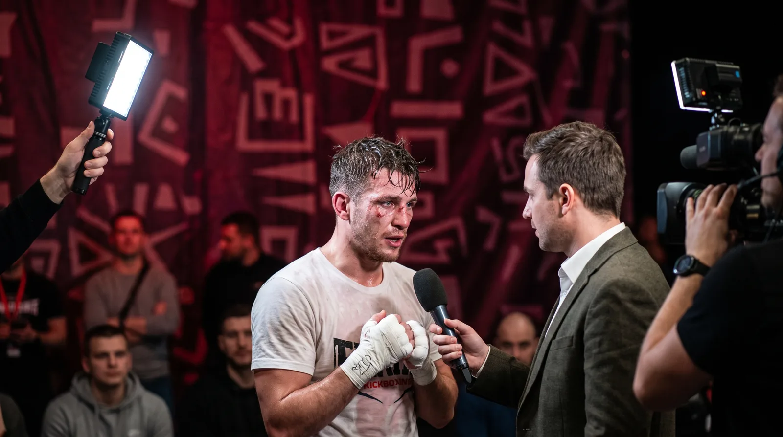 Entrevista con micrófono a un peleador con vendas al terminar su combate, frente a un photocall