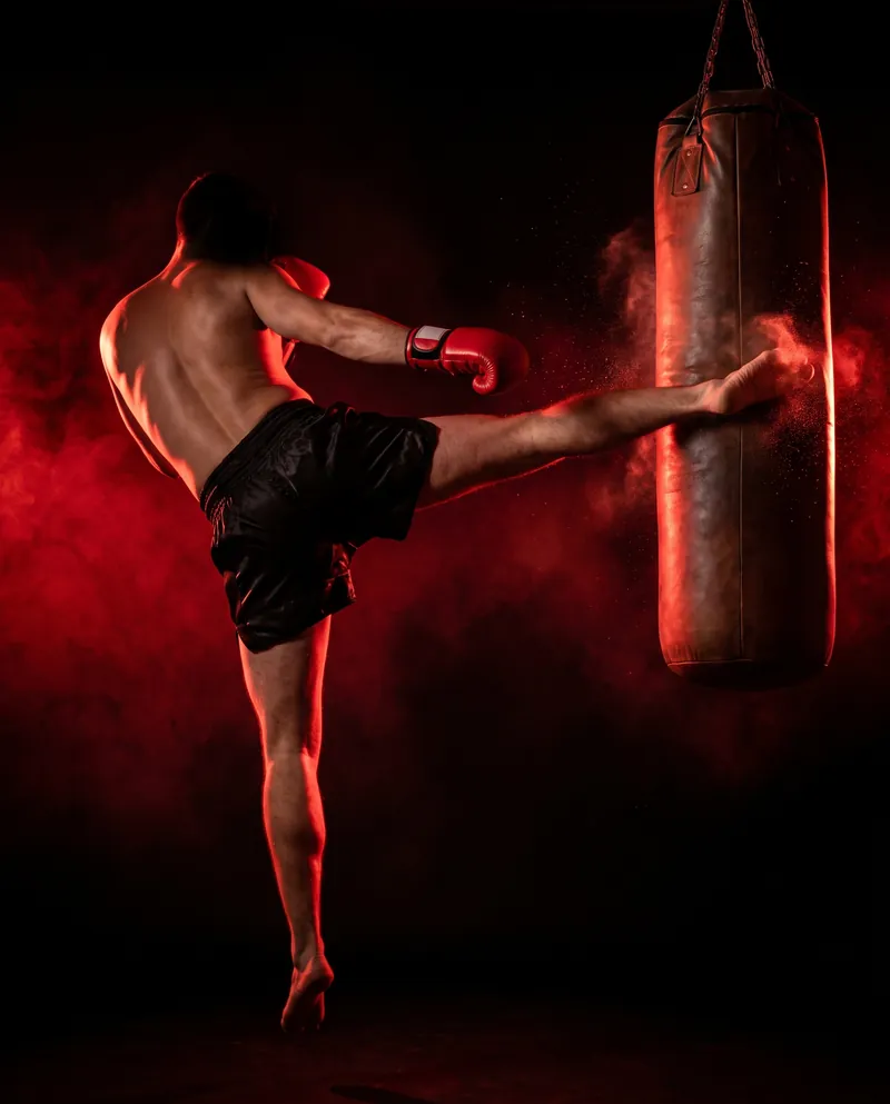 Kickboxer de espaldas lanzando una patada circular al saco bajo luz roja