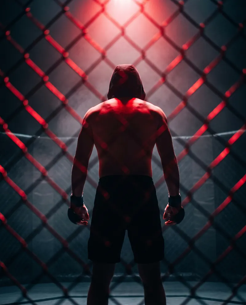 Luchador de mma de espaldas tras la malla de la jaula iluminada en rojo